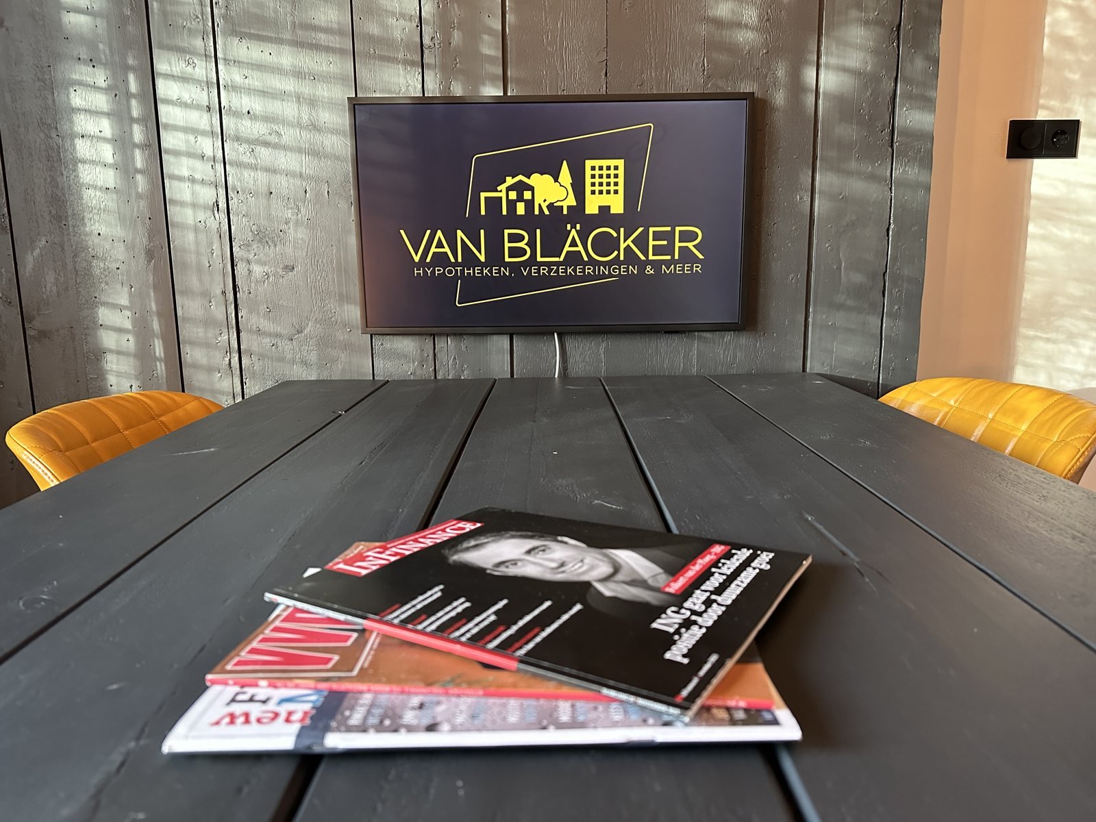 Gesprekstafel met gele stoelen en het Van Bläcker-logo in ons kantoor