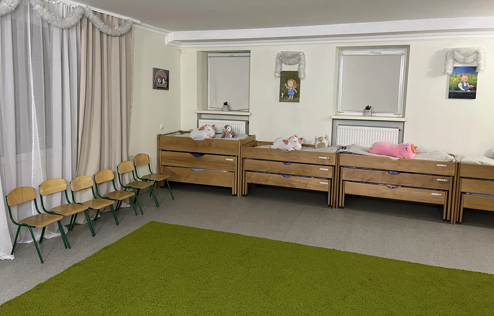 Групова кімната в укритті садочка Unique Kids: зелений килим, дитячі стільці, висувні ліжка для денного сну