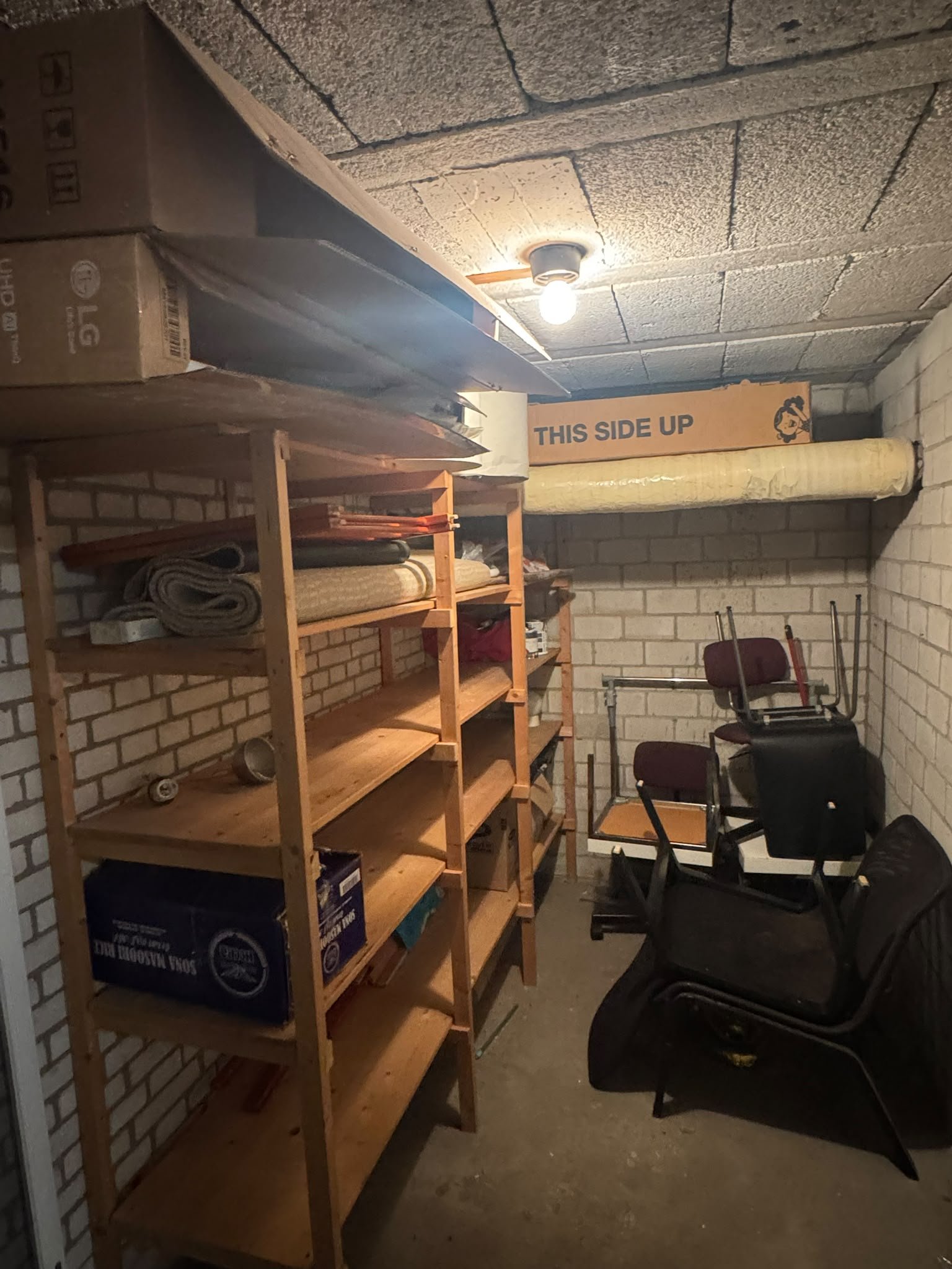 Een kelder met rekken, stoelen en opgeslagen spullen.